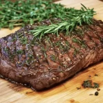 Seasoned venison steak with fresh herbs on a wooden board